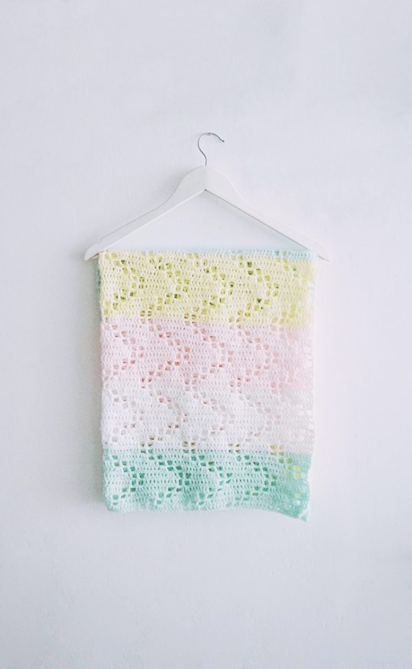 a colorful crochet baby blanket hanged on a white wall