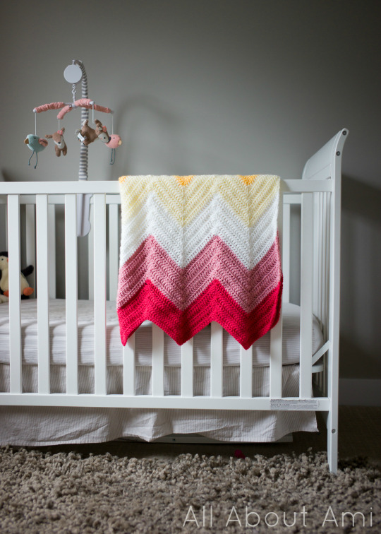 A bright chevron crochet blanket beside a baby crib
