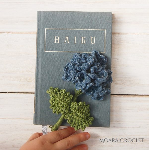 person holding a book with crochet hydrangea flower